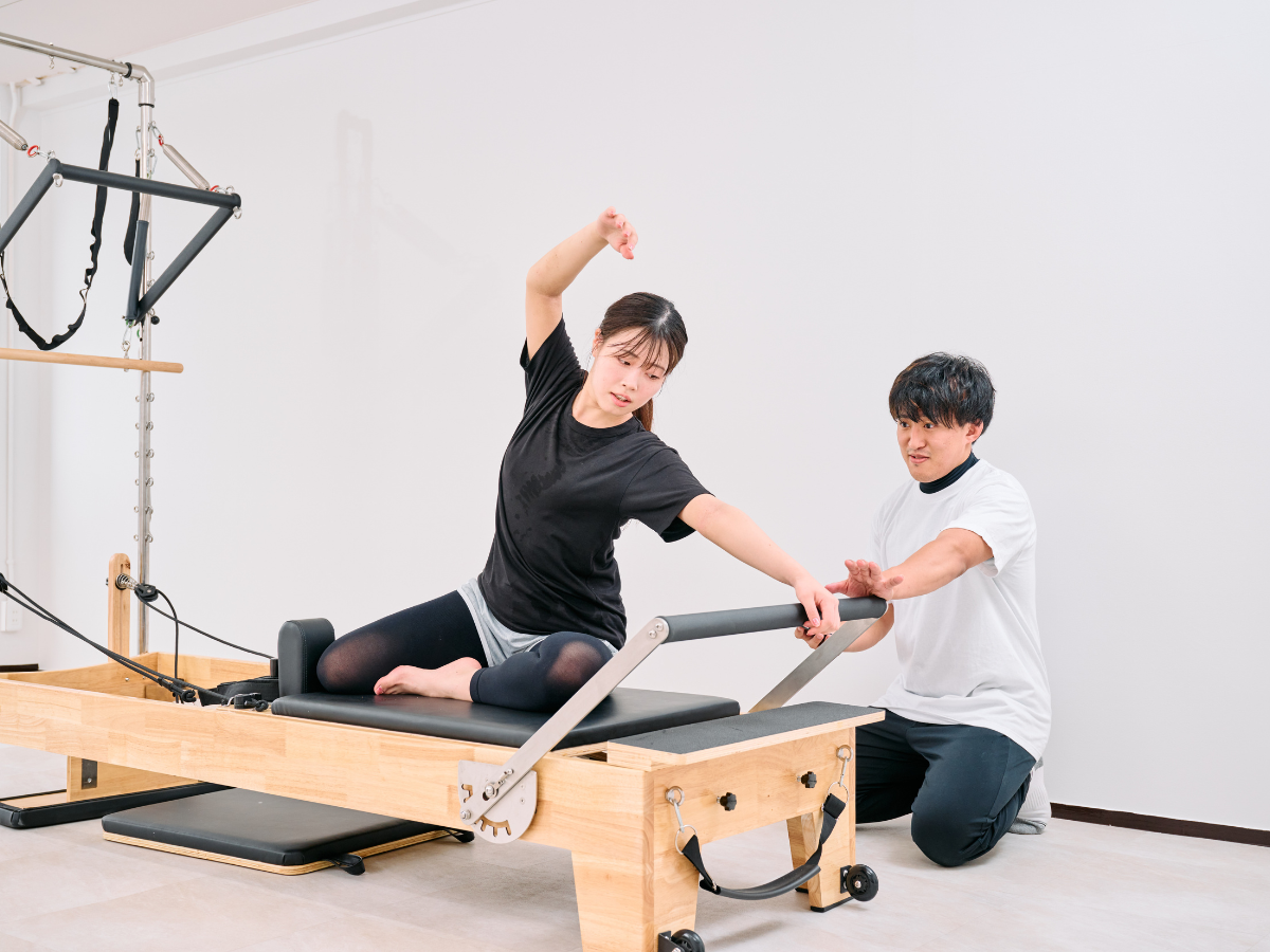 トレーナーのサポートでマシンピラティスを行う様子